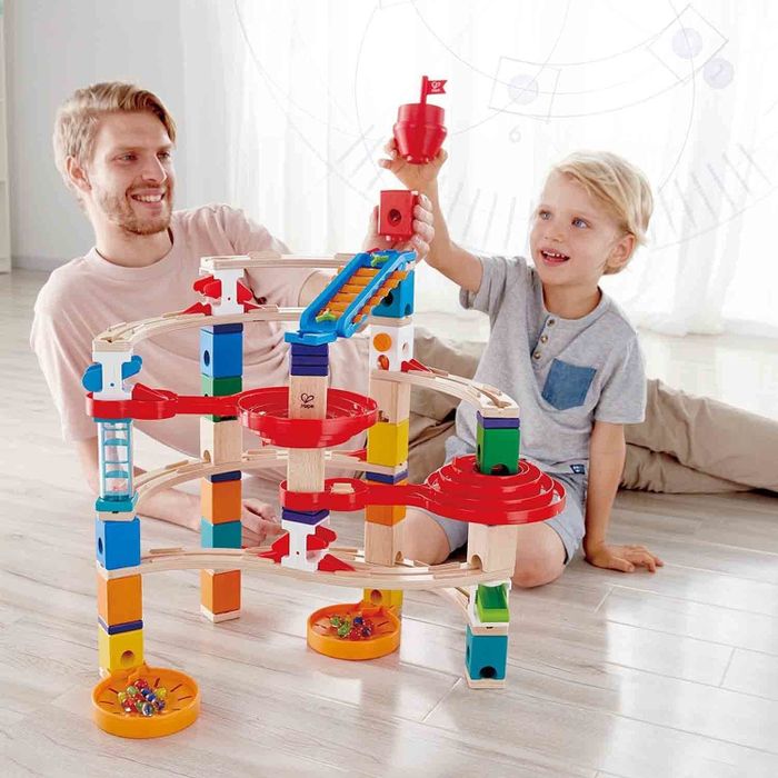 A photo showing an adult and child joyfully playing with a block set and marbles.