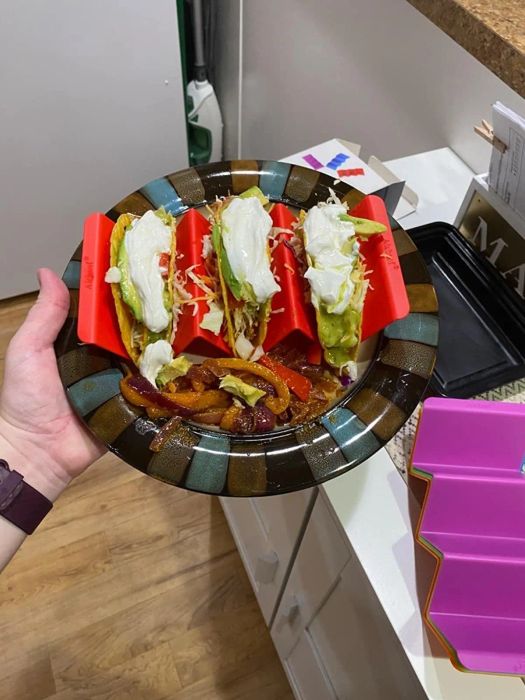 A hand holding a plate with red taco holders filled with shelled tacos, ready to be served.