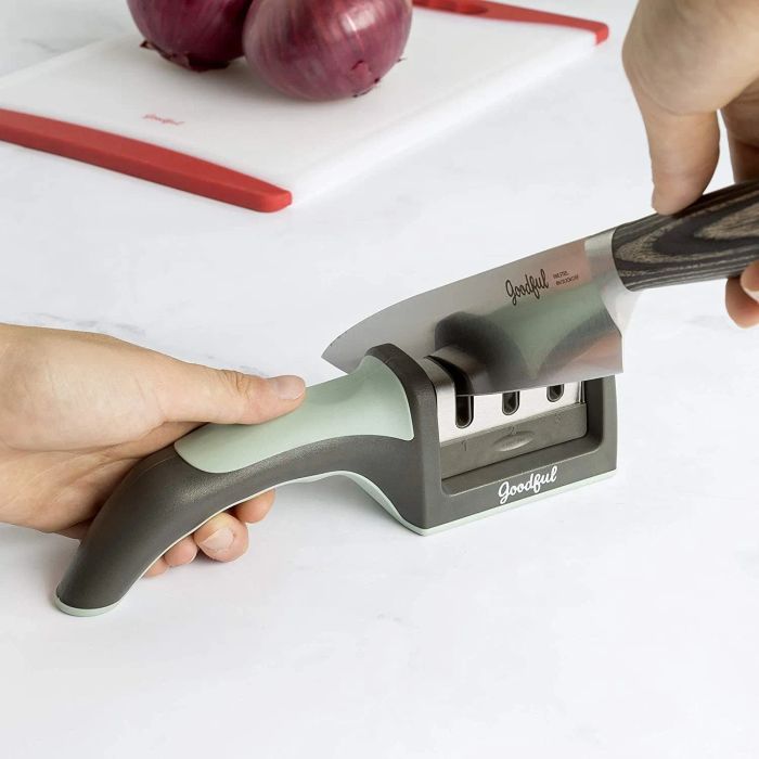 A hand demonstrating the green Goodful knife sharpener, honing a large silver knife to perfection.