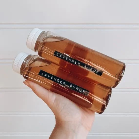 A pair of hands holding bottles of lavender simple syrup, ready to be poured into drinks or baked treats for that extra touch of flavor.