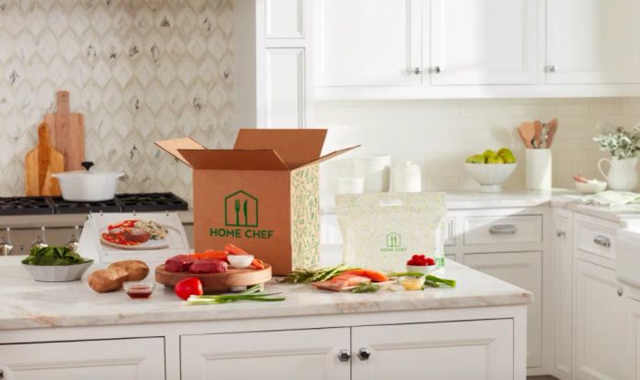 A HomeChef box filled with recipe ingredients like vegetables, meat, and fish, alongside a booklet of recipe cards, all laid out on a kitchen counter