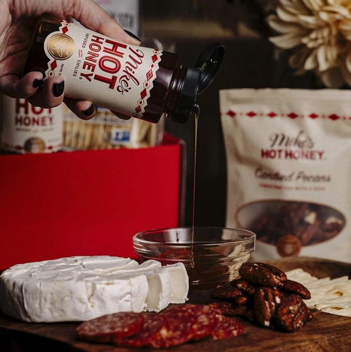 Hand drizzling Mike's Hot Honey over a slice of charcuterie sausage.