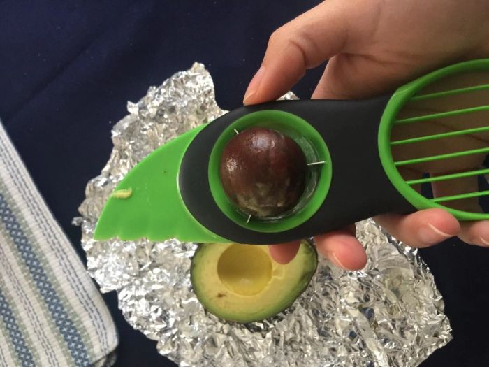 A reviewer holding a green avocado slicer that has removed the pit from an avocado, ready to be sliced
