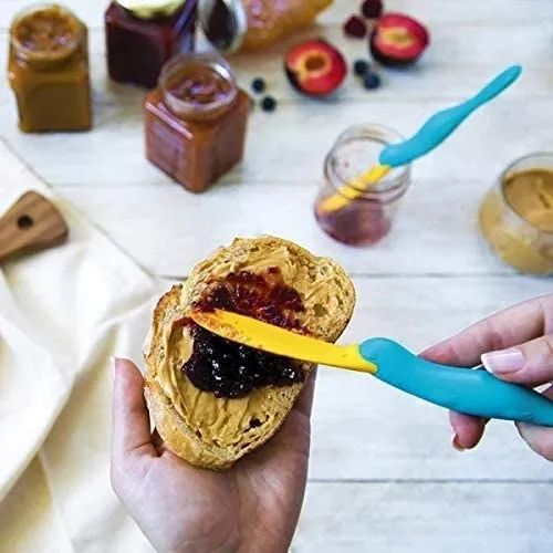 Hand using a platypus-shaped jar scraper spatula to spread jam on a piece of bread with peanut butter