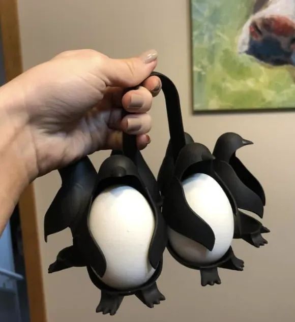 Hand holding a penguin-shaped egg cooker with eggs nestled inside the penguin's bellies