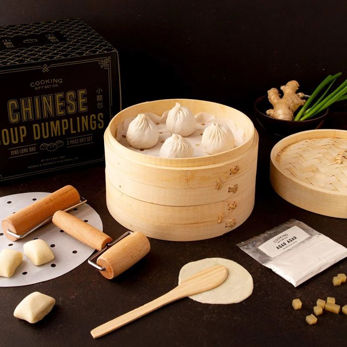 Soup dumplings arranged in a wooden basket with tools and dough scattered around, ready for the next step in the dumpling-making process.