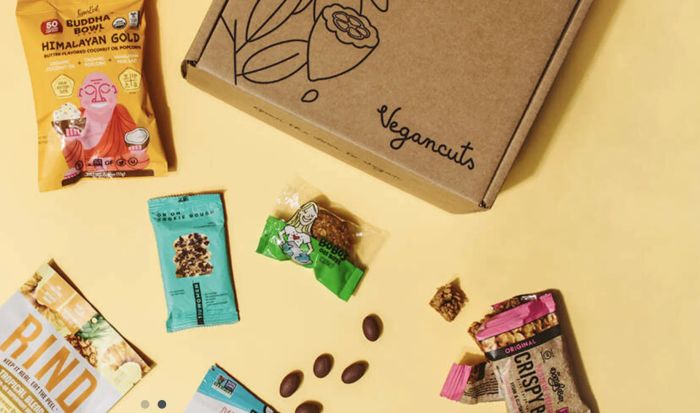 A Vegancuts subscription box placed next to a variety of vegan popcorn and snack bars