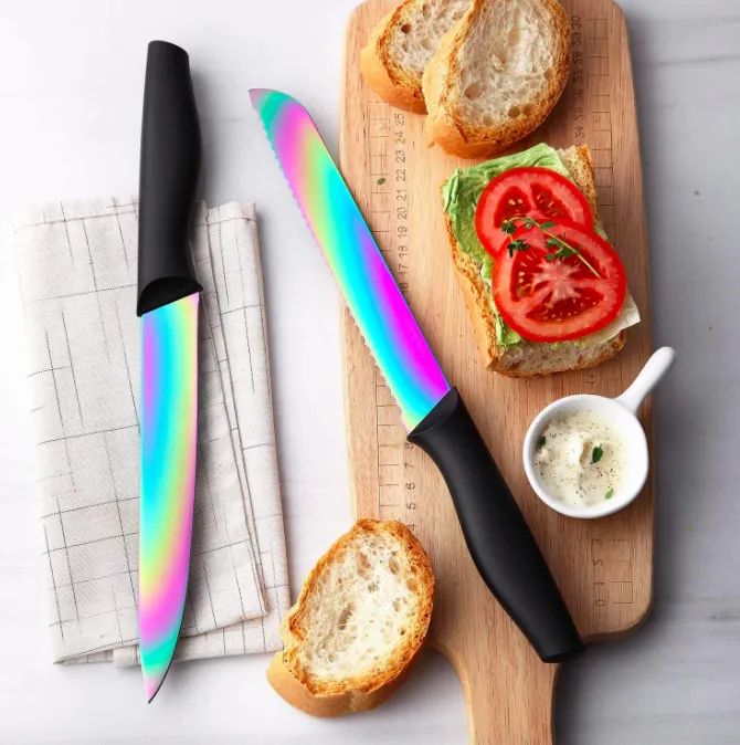 A set of iridescent rainbow knives with black handles placed next to a cutting board with sliced bread