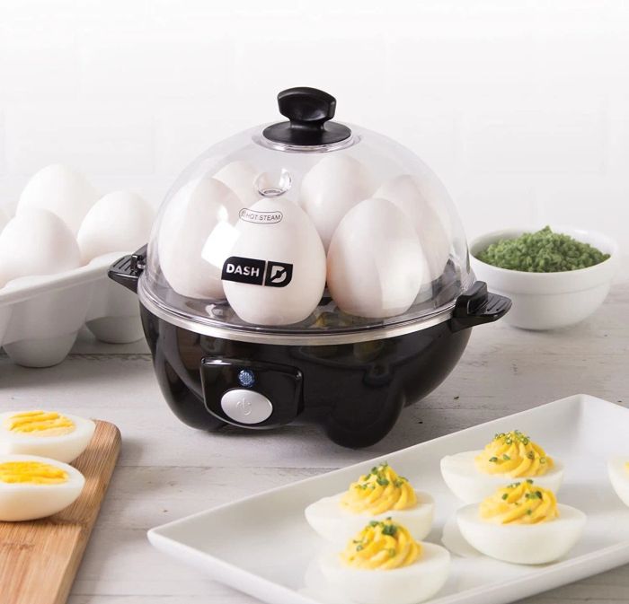 A black Dash Rapid Egg Cooker heating six hard-boiled eggs on a table.