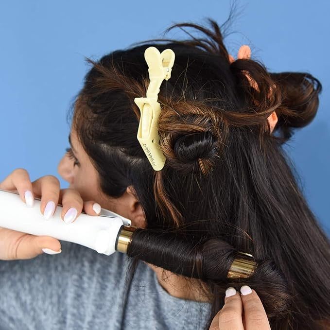 A person curling their hair with a curling iron, holding a section in place with a yellow clip