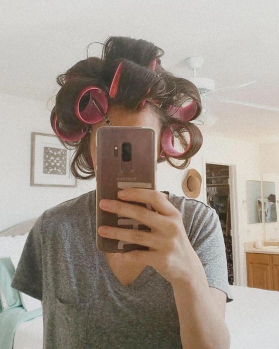 A person with hair in rollers taking a selfie, reflecting modern beauty trends