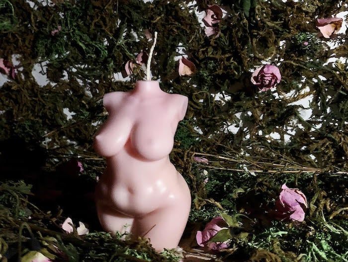 A candle shaped like the bust and torso of a naked woman, in a soft pink hue.