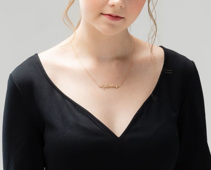 A model showcasing a golden single-chain necklace with a pendant that reads 'love,' flanked by EKG lines on both sides.