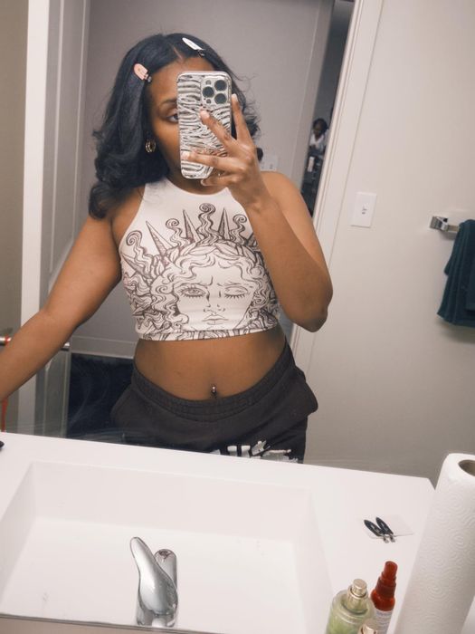 A person in a graphic-print crop top and sweatpants taking a mirror selfie with no-crease hair clips