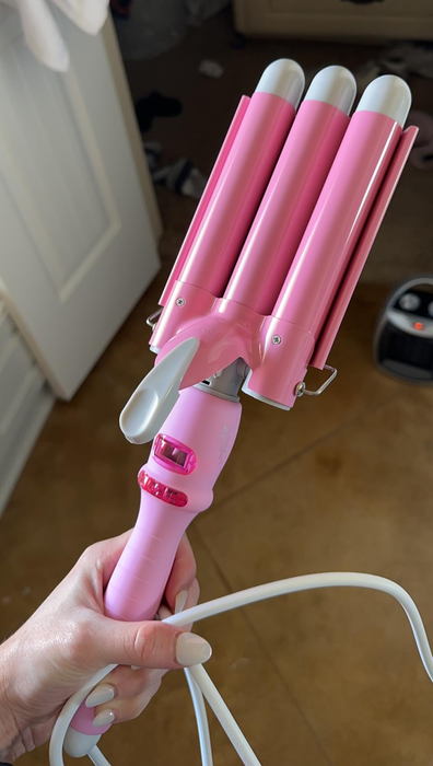 A person holding a pink hair-waving styling tool