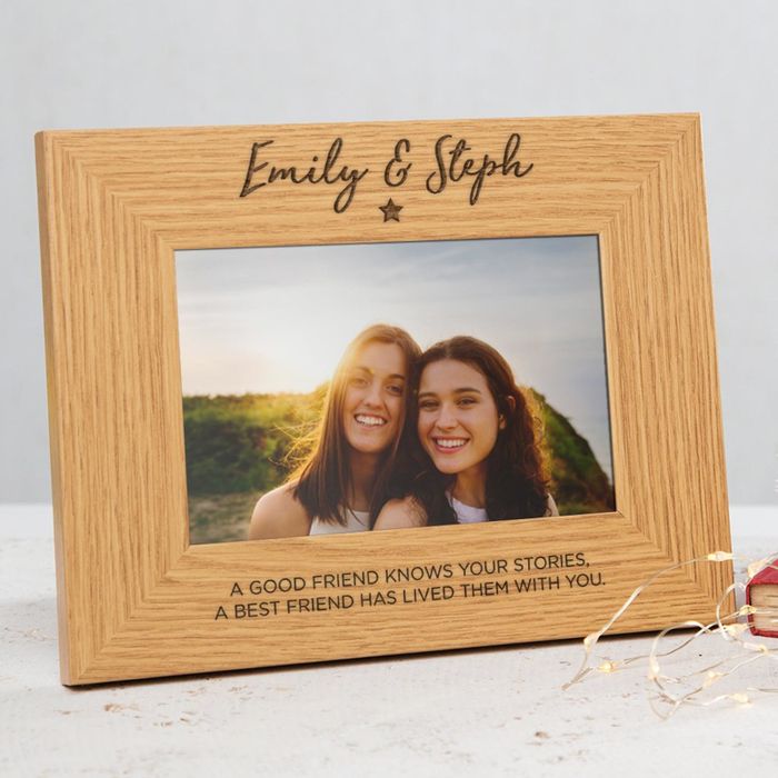 A wooden picture frame with the names "Emily and Steph" elegantly etched at the top, accompanied by a heartwarming message below: "A good friend knows your stories. A best friend has lived them with you."
