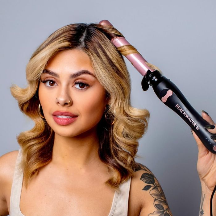 A woman styling her shoulder-length hair with a curling wand.