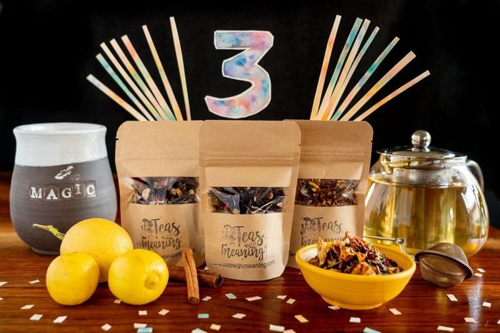 A tea bundle featuring a clear kettle of tea, whole lemons, three tea bags, a bowl of loose leaf tea, a steeper, and a cozy mug.