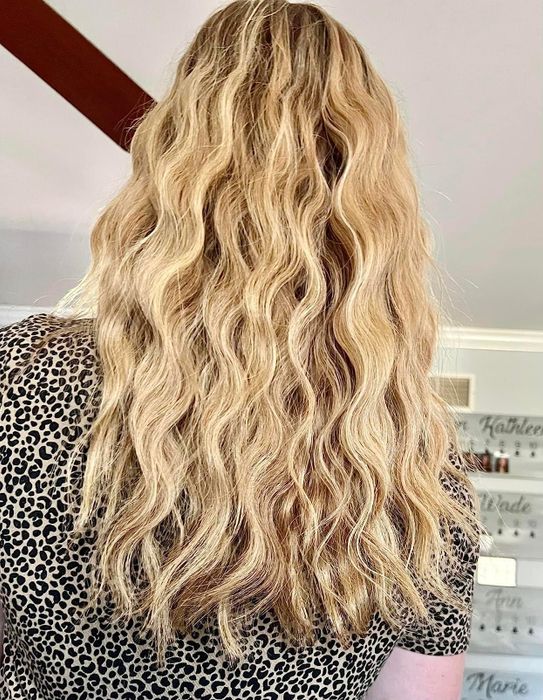 A person with long, wavy blonde hair, wearing a leopard print top, seen from behind