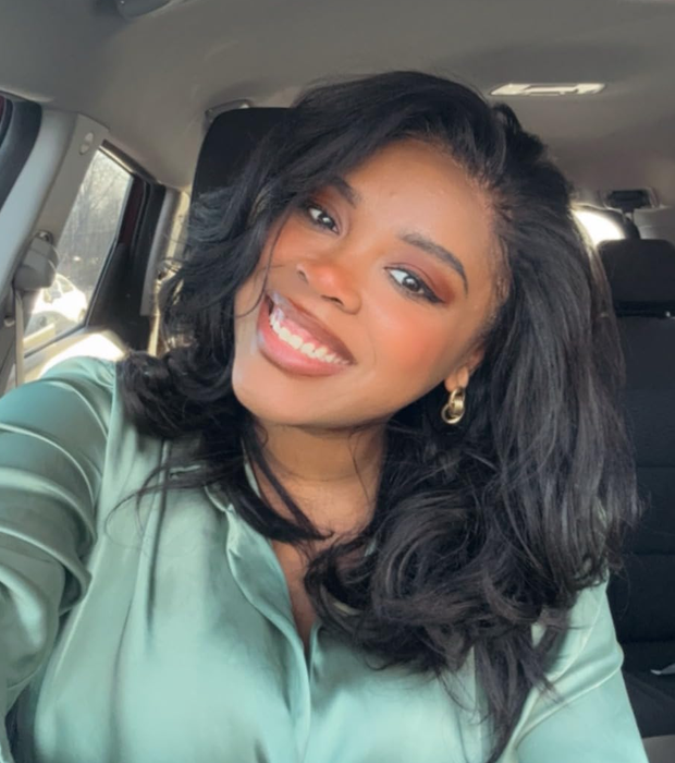 A woman smiling in a car, wearing hoop earrings and a green blouse