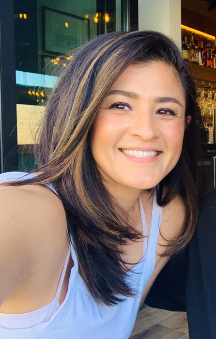 A woman smiling in a white tank top, casually posing for a photo.