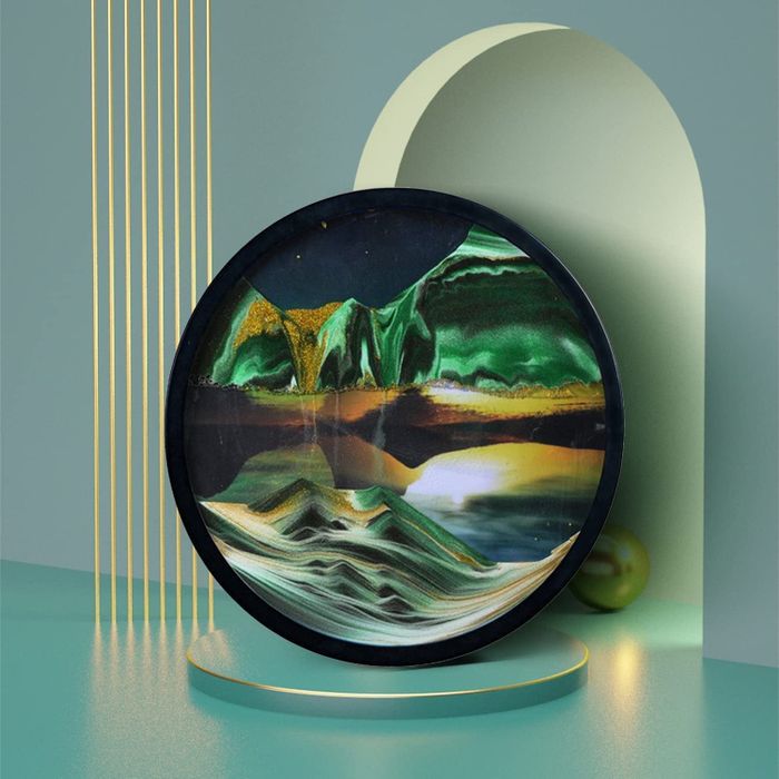 A round glass frame with sand inside that forms two distinct mountain shapes as it moves.