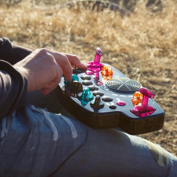 A person holding a colorful, retro-inspired portable gaming console outdoors, dressed in ripped jeans.