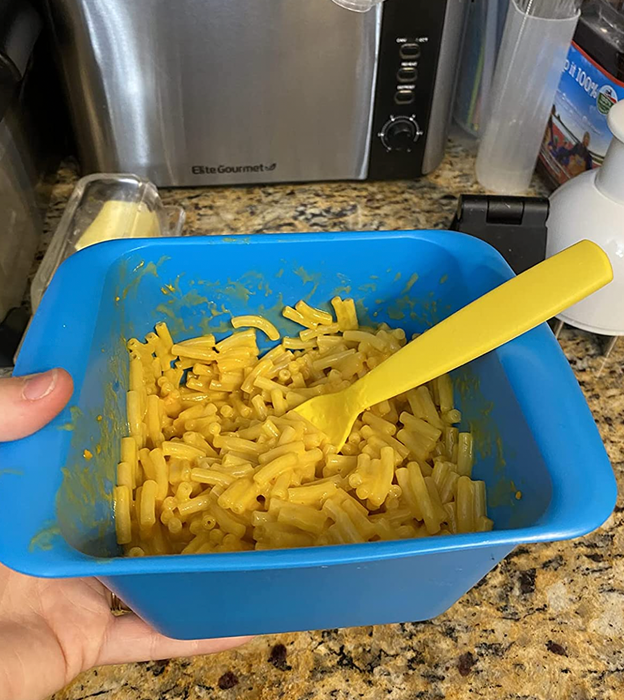 A reviewer holding a blue, square-shaped silicone cooker filled with mac and cheese