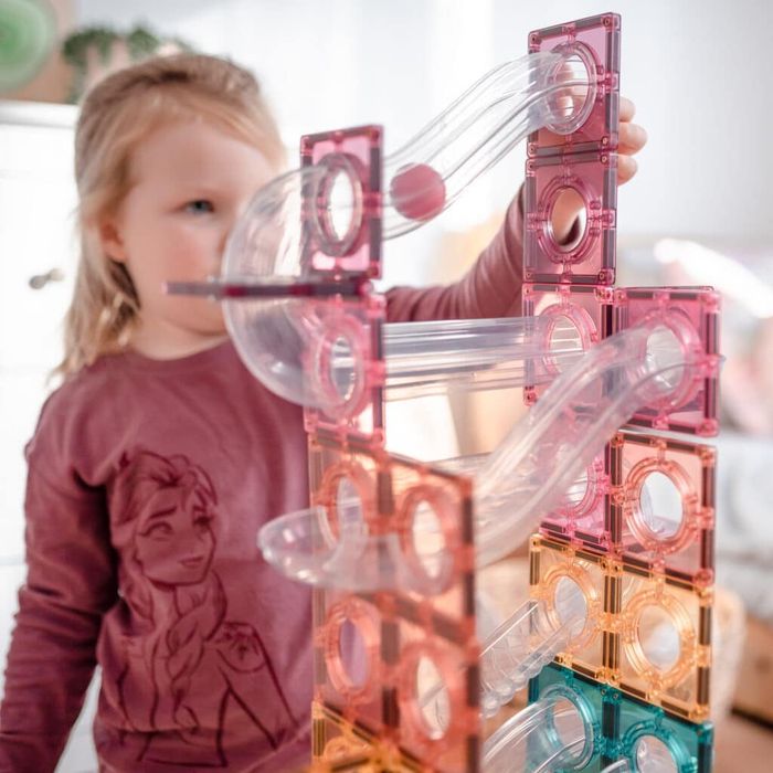 A child enjoys building with a colorful magnetic tile set, wearing a shirt featuring Elsa from Frozen