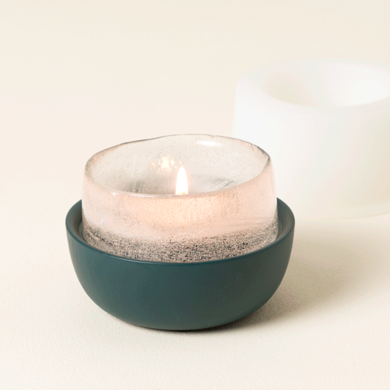 A lit candle with a frosted glass holder placed in a sleek dark bowl, perfect for home decor lovers
