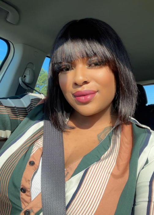 A person sitting in a car, wearing a striped outfit and sporting a chic hairstyle, while safely buckled up with a seatbelt.