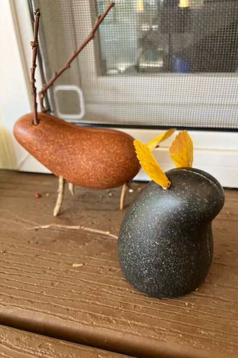 Two bird-inspired sculptures crafted from smooth stones, twigs, and leaves, placed on a wooden shelf.