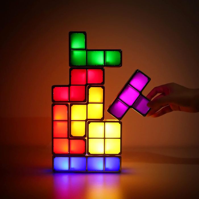 A hand arranging colorful, Tetris-shaped LED blocks into a glowing stack.