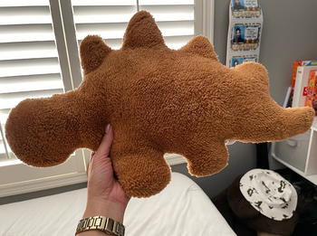 A reviewer proudly showing off their stegosaurus nugget pillow, a fun and playful addition to any space.