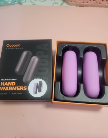 Ocopa rechargeable hand warmers in purple, displayed with their packaging in a shopping article.