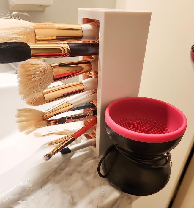 The cleaning tool rests next to a container with a reviewer’s brushes drying, showing the silicone bristles at the bottom of the spinning bowl.