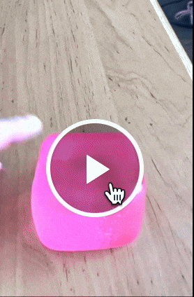 reviewer squeezing a pink, see-through, square-shaped stress ball