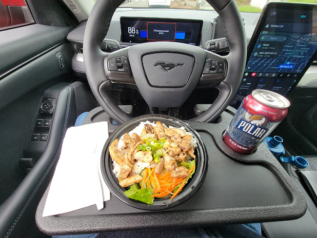 A reviewer's tray is attached to the steering wheel, holding a fresh lunch — a salad in the center and a soda resting in the cup holder.