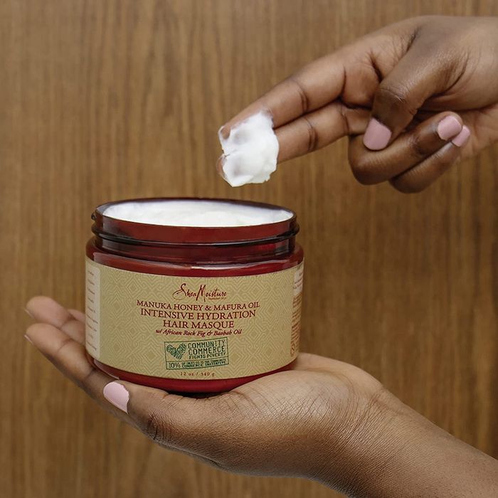A model is shown scooping the hair mask from a red container.