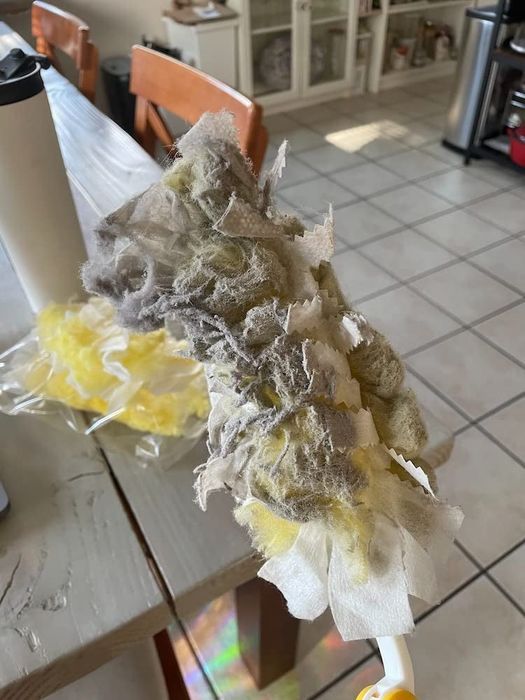 A dusty and dirty cleaning duster held over a kitchen floor.