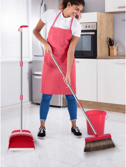 A woman in an apron sweeps her kitchen floor with a broom, accompanied by a dustpan and bucket. Featured in a shopping article.