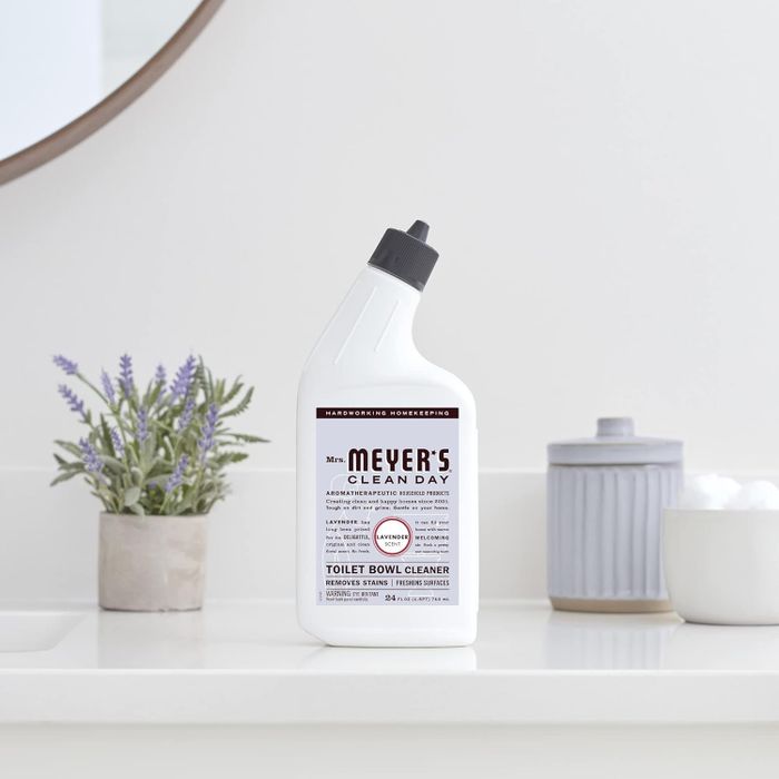 A bottle of Mrs. Meyer's Clean Day toilet bowl cleaner sits on a bathroom counter next to natural decor.