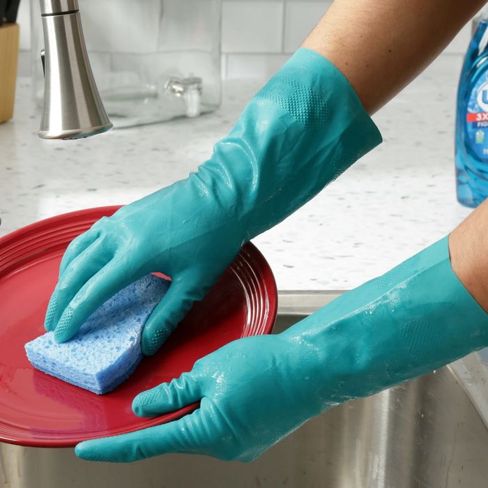 A person wearing rubber gloves scrubbing a plate with a sponge in a kitchen