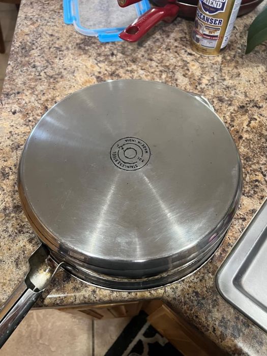 A stainless steel pan rests upside down on a kitchen counter, with a jar of cleaner placed in the background.