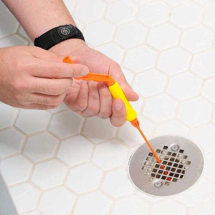 A hand feeds a drain snake down the drain and twists the handle to maneuver it.
