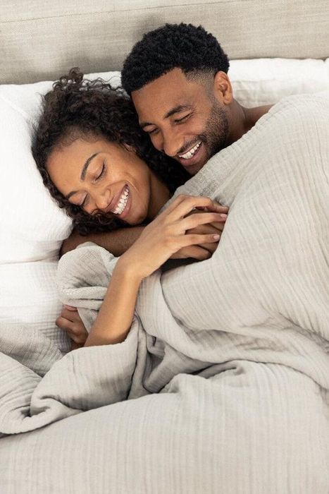 two models cuddling in bed under a cream-colored blanket