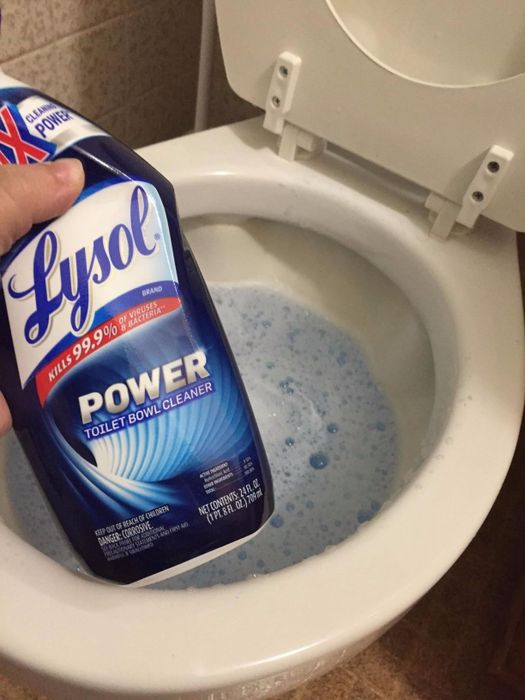 The reviewer holds a bottle of Lysol Power Toilet Bowl Cleaner above an open toilet bowl, filled with blue gel.