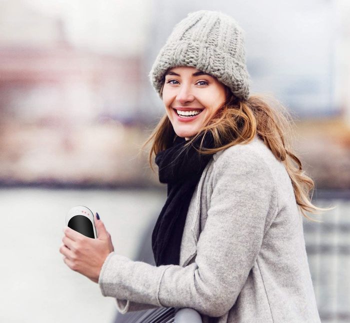 a model smiling while holding the Infray hand warmer in their left hand on a cold day