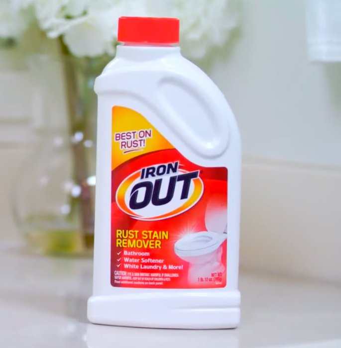 A bottle of Iron OUT rust stain remover sits on a bathroom counter.