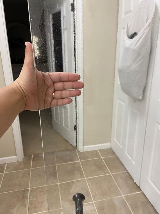 The same shower door with the reviewer's hand, but this time the door is completely clear and spotless.